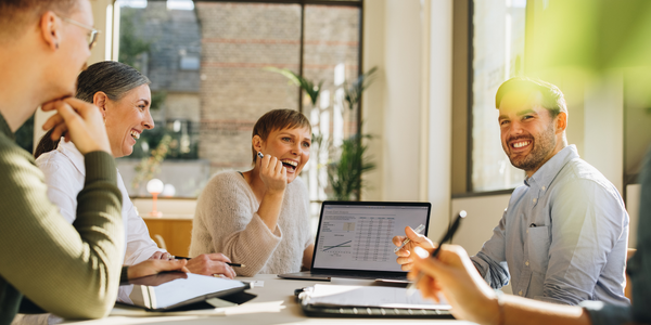 Group of employees sat at desk smiling looking at laptop screen