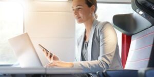 Woman on train holding her phone and working on laptop