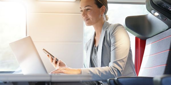 Woman on train holding her phone and working on laptop