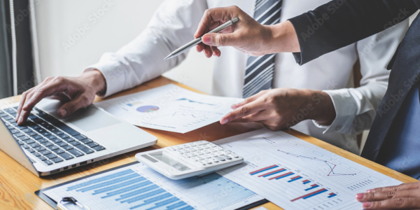 Arms and hands working away with spreadsheets, graphs and calculators on a table