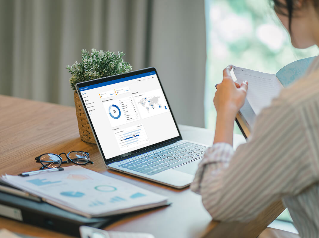 User analyzing financial reports with a Webexpenses dashboard open on a laptop screen and printed documents on the desk.