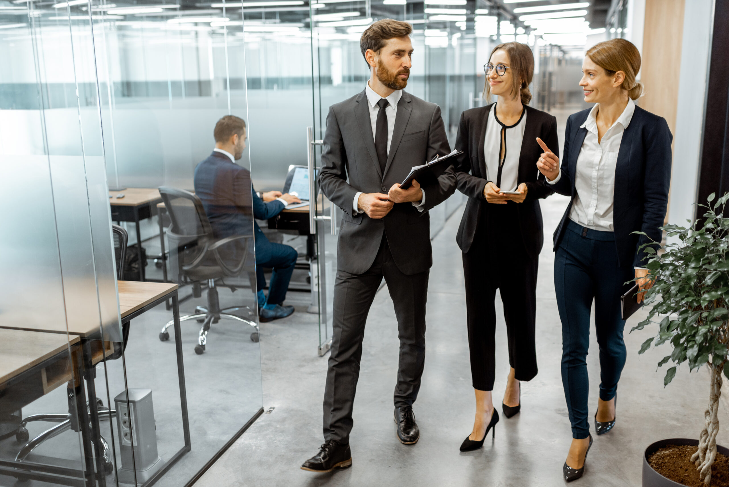Business people walking in the hallway of the modern office building with employees working behind glass partitions. Work in a large business corporation
