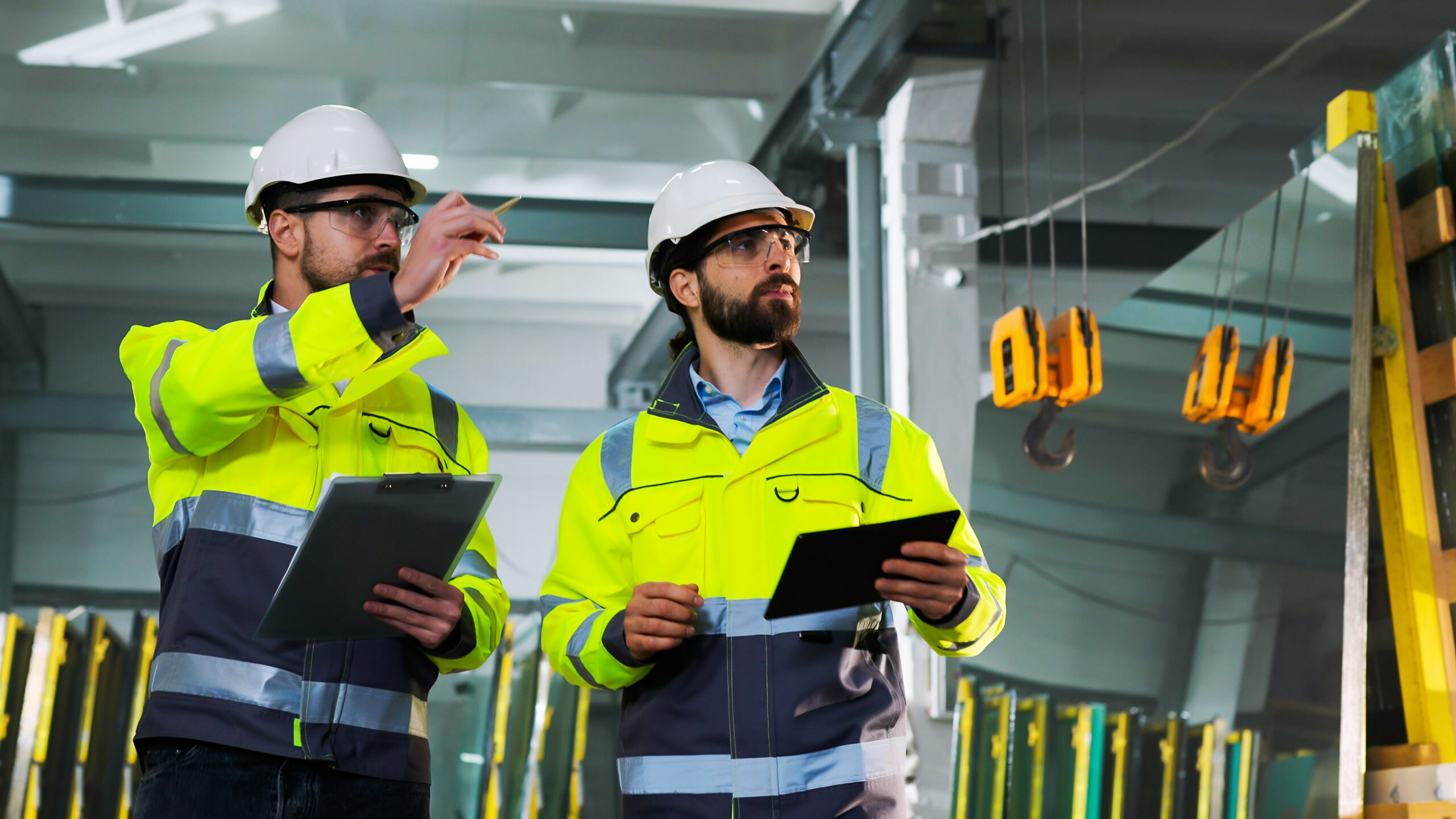 Caucasian men colleagues talking and planning work. Males walking at factory. Work with folder of documents and tablet device at manufactory. Production co-working. Discussion of technicians indoors.