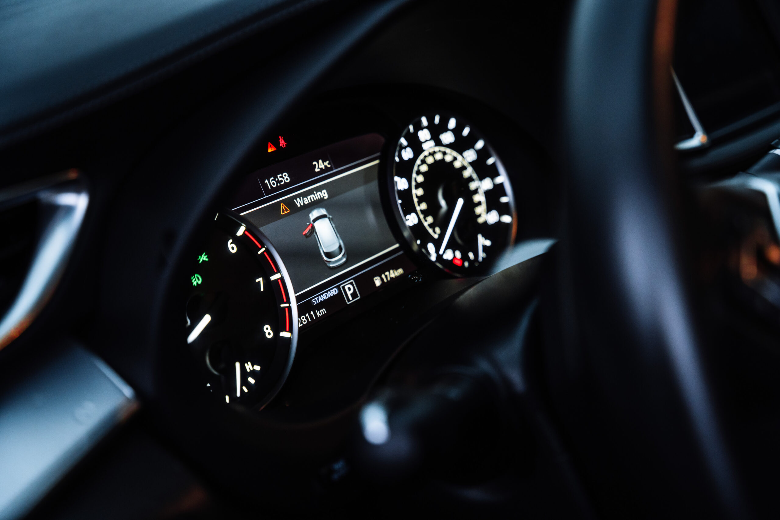 Close-up view of a modern car interior featuring illuminated digital instrument cluster and dashboard controls. Automotive technology concept showing speedometer, warning display, driving information, and premium vehicle cockpit design in low light conditions.