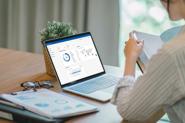 User analyzing financial reports with a Webexpenses dashboard open on a laptop screen and printed documents on the desk.