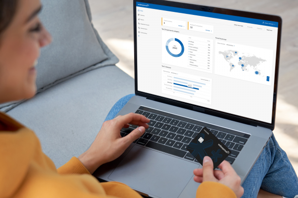 Woman with laptop on her lap, with Expense Card in one hand, typing into Webexpenses system with the other